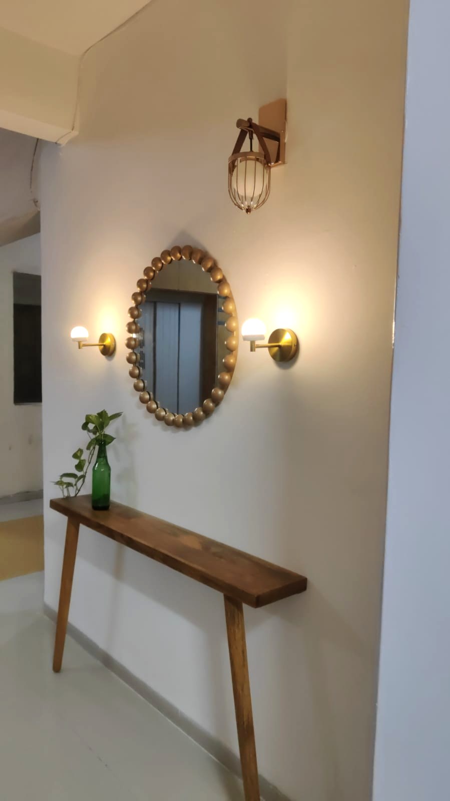 Warm entryway designed with a sculptural mirror, brass lighting, timber console and greenery